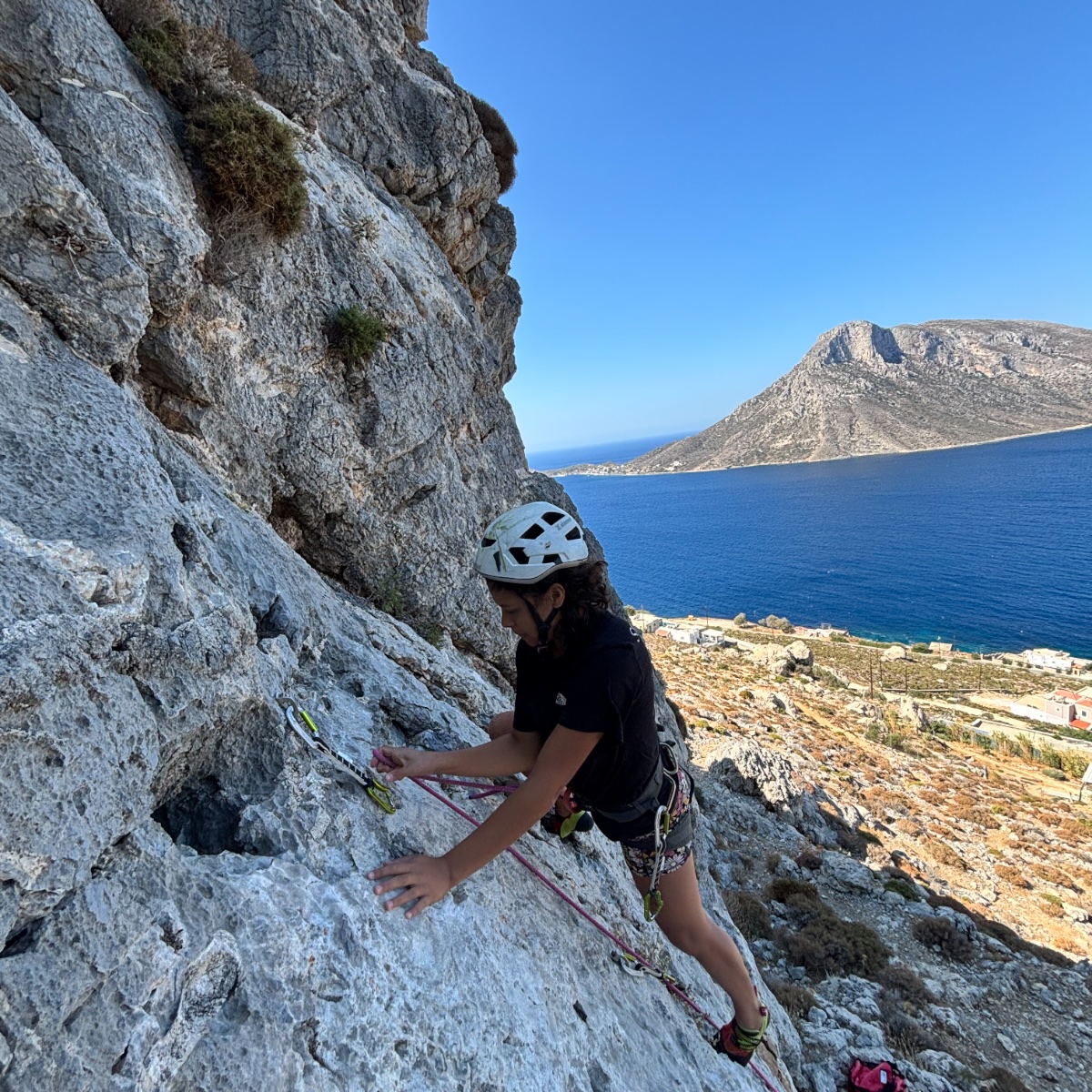 Maria climbing a limestone wall high above a blue bay