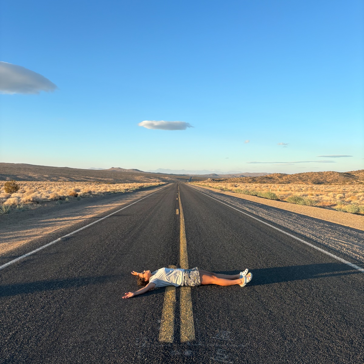 Maria lying flat in the middle of an empty desert highway