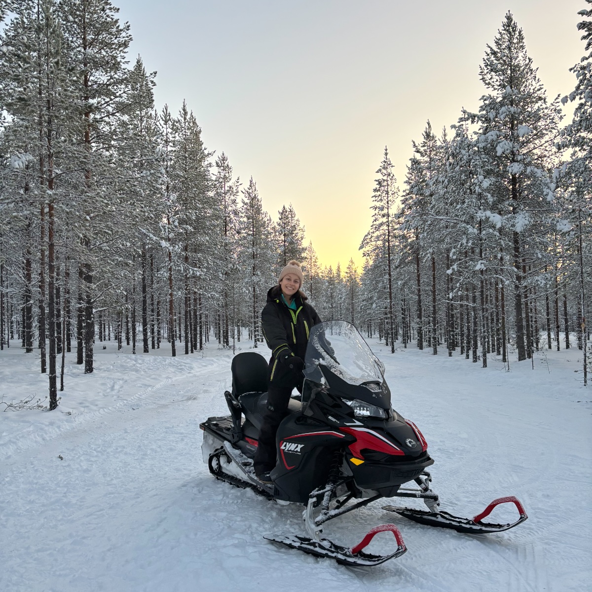 Maria on a snowmobile in a snowy forest at golden hour