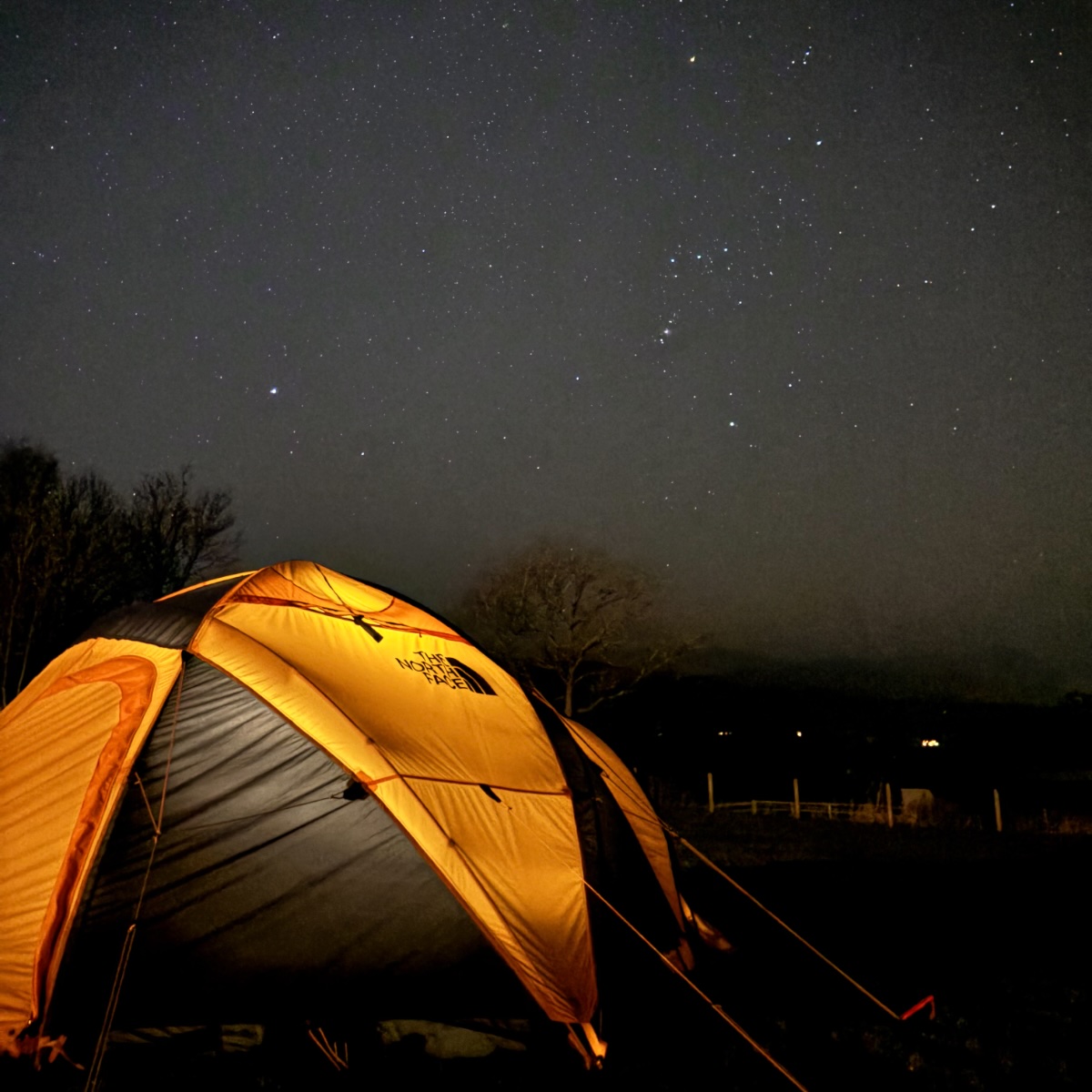 A glowing tent under a sky packed with stars